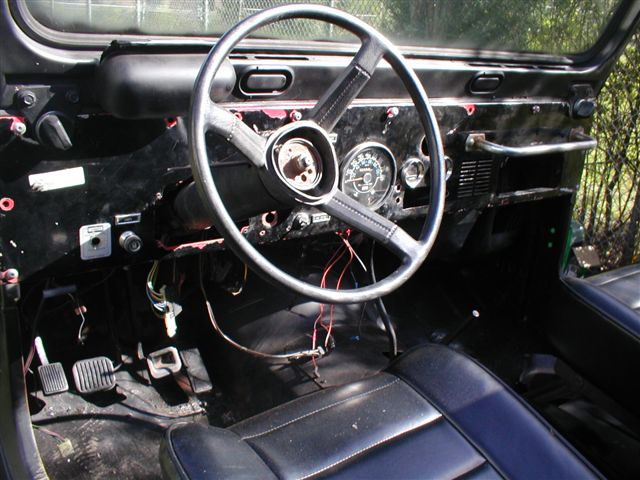 Jeep CJ interior showing dashboard, steering wheel, pedals, and seats. Wiring is exposed