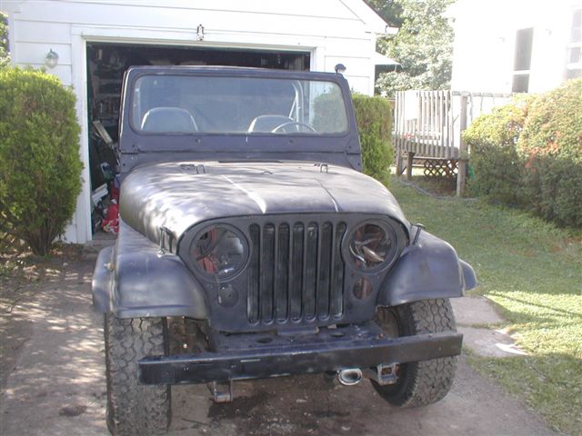 Front view of a dark-colored Jeep CJ-5 parked in front of a garage