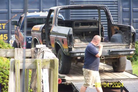 1979 Ford Bronco II - A man stands near a weathered 1979 Ford Bronco being transported on a trailer, with another vehicle visible behind it.