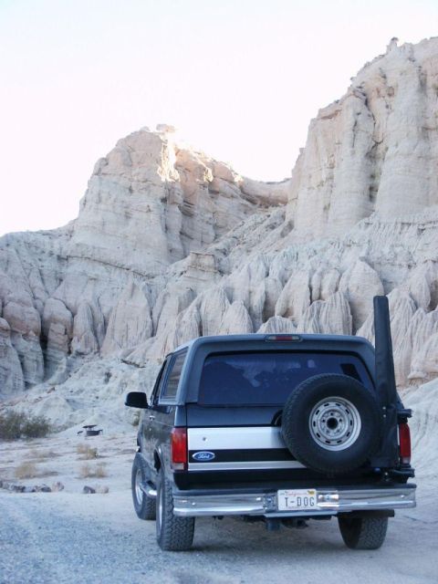 1996 Ford Bronco - A black Ford Bronco is parked on a dirt road with a backdrop of large rock formations.