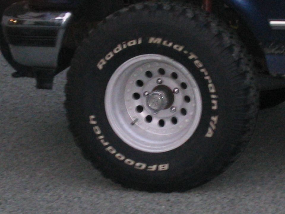 Silver steel wheel with BFGoodrich Mud-Terrain T/A tire on a blue truck.