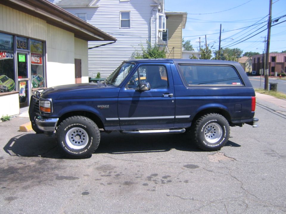 Dark blue Ford Bronco side profile on BFG Mud-Terrains outside a speed shop