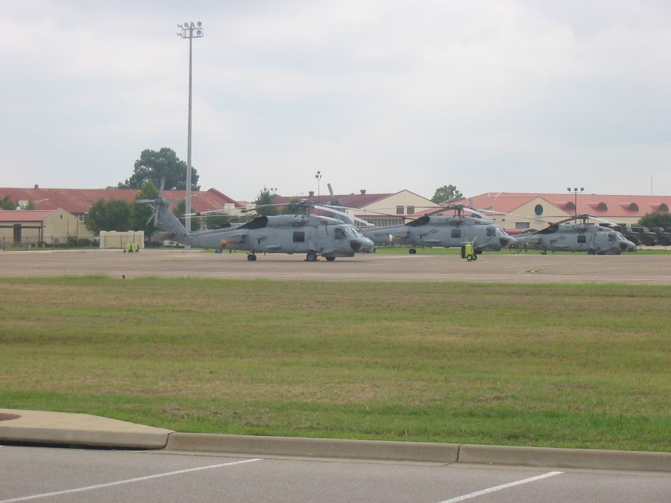 Several military helicopters parked on an airfield with buildings in the background