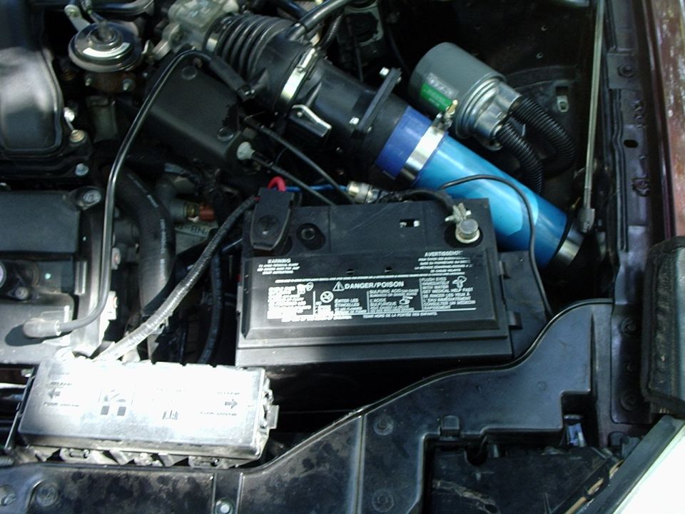 engine bay showing battery, fuse box, and blue intake pipe