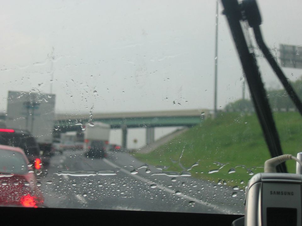 View through a rain-streaked windshield of a highway traffic jam with trucks and cars