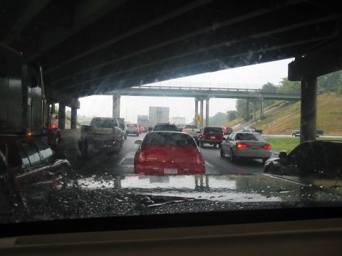 1988 Ford Bronco - A view from inside a vehicle shows a traffic jam on a wet highway under an overpass with multiple cars and trucks.