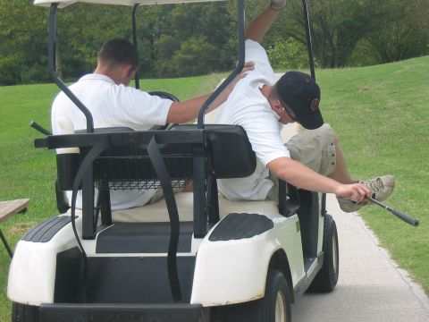 1988 Ford Bronco - Two men are riding in a golf cart on a sunny day, with one man's legs extended out of the vehicle.