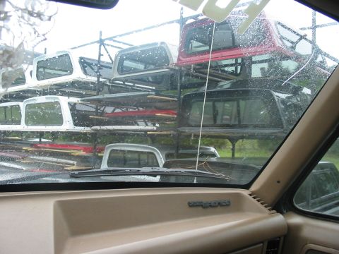 1988 Ford Bronco - View from inside a 1988 Ford Bronco shows a rack filled with various truck caps on a rainy day.