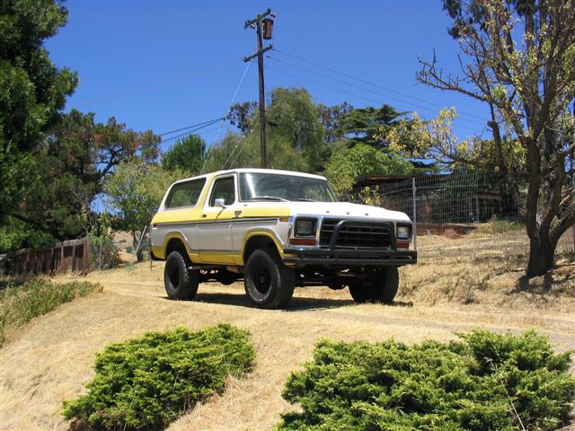 White and yellow Ford Bronco SUV on dirt path with brush guard and lift kit