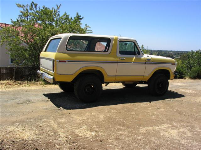 Yellow and white 1970s Ford Bronco with white hardtop, rear three-quarter view