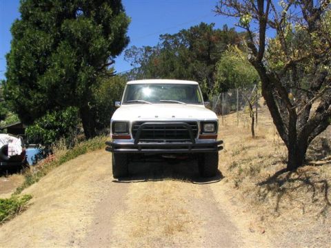 1978 Ford Bronco - A white 1978 Ford Bronco is parked on a dirt road, surrounded by trees and dry grass.