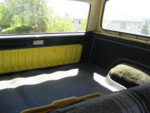 1978 Ford Bronco - The rear interior of a vehicle shows yellow ribbed paneling and black trim, with a gray mat on the floor.