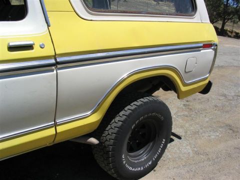 1978 Ford Bronco - The rear quarter panel of a two-tone yellow and white 1978 Ford Bronco, highlighting its distinctive body style and chrome accents.