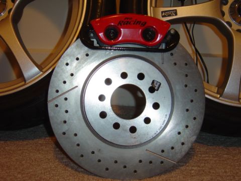 1998 Ford Taurus - A drilled brake rotor and red performance caliper are shown, with a portion of a gold wheel in the background.