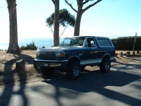 1990 Ford Bronco - This lifted 1990 Ford Bronco is parked near the coast with trees and the ocean in the background.