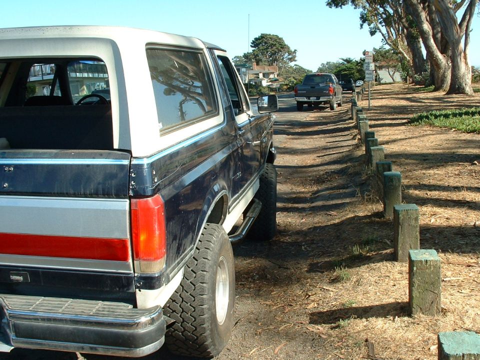 Dark blue and white Ford Bronco with a lift kit parked on a dirt road