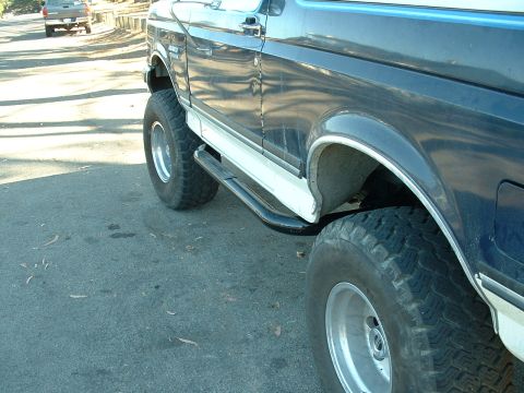 1990 Ford Bronco - Side view of a lifted 1990 Ford Bronco, showing its running boards and off-road tires.