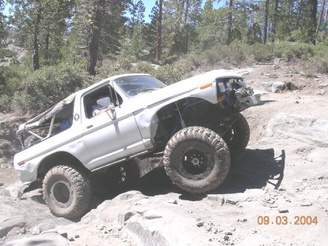 1994 Ford Bronco - This modified SUV navigates a challenging rocky trail, its body showing signs of off-road use.