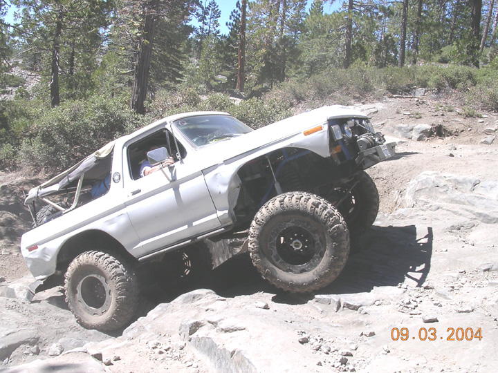 Doorless white Ford Bronco rock crawler with winch flexing over granite, 2004