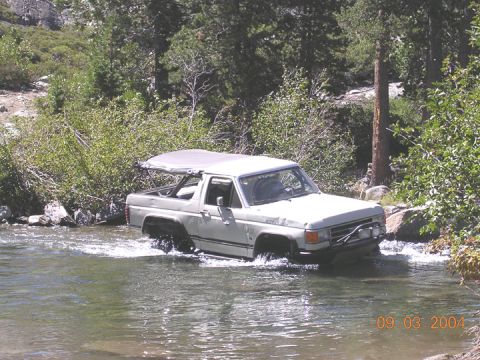 1994 Ford Bronco - A white 1994 Ford Bronco navigates a river crossing, its soft top deployed.