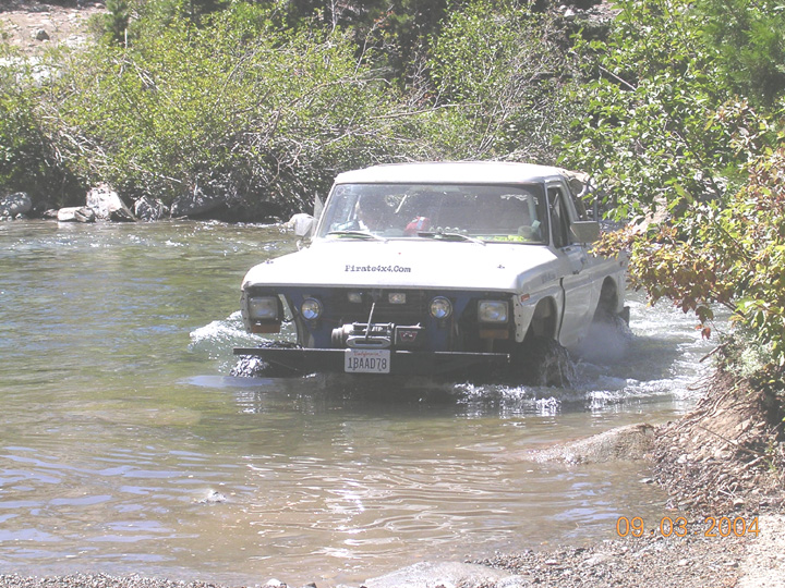 White lifted truck with winch and 'Firsts4x4.com' lettering crossing a shallow river