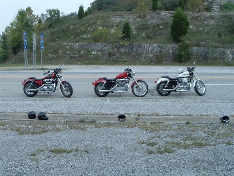 1995 Mercury Grand Marquis - Three motorcycles are lined up on the shoulder of a road with highway signs in the background.