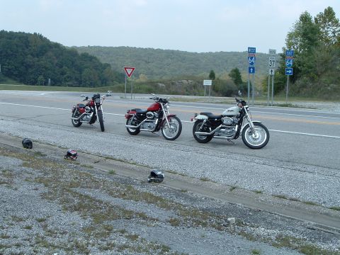 1995 Mercury Grand Marquis - Three motorcycles are parked on the side of a highway, with helmets laid out on the ground beside them.