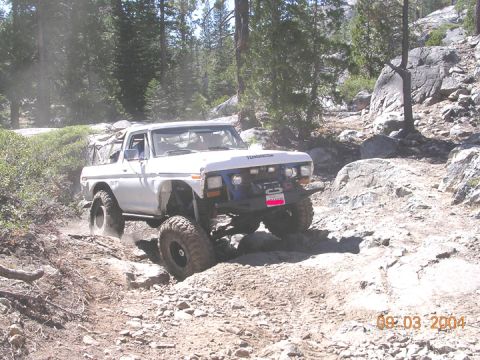 1994 Ford Bronco - A modified white SUV tackles a challenging rocky terrain on a sunny day.