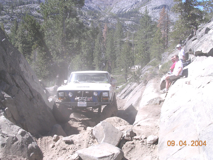 White Ford Bronco with winch bumper crawling granite boulders on a mountain trail, 2004