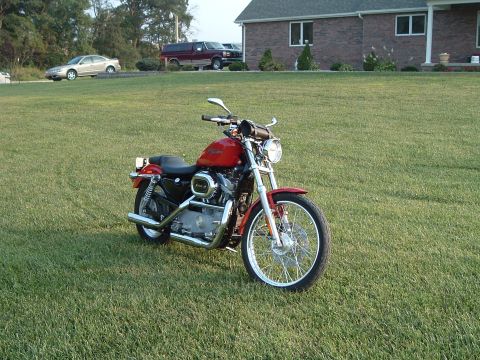 1995 Mercury Grand Marquis - A red motorcycle sits on a green lawn with a house in the background.
