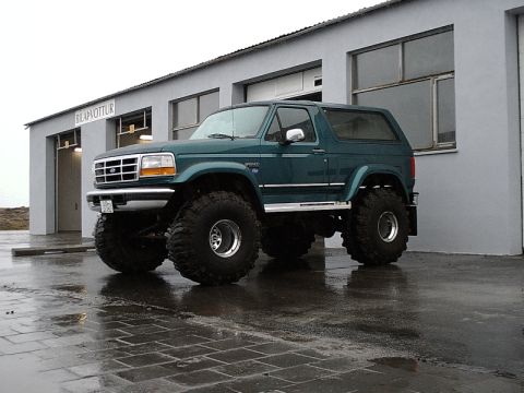 1996 Ford Bronco - A modified 1996 Ford Bronco with large off-road tires sits outside a building on a rainy day.