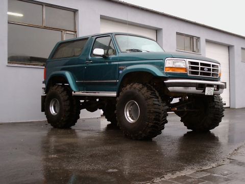 1996 Ford Bronco - This lifted 1996 Ford Bronco features oversized tires and a distinctive green paint job, parked outside a garage on a wet day.