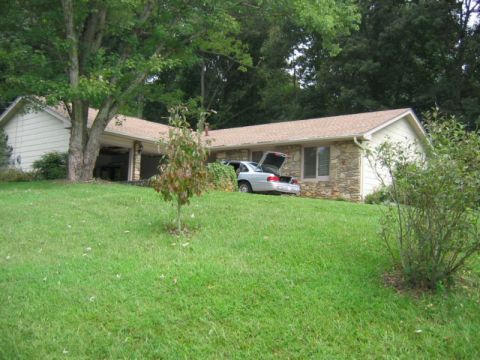 1985 Ford LTD Crown Victoria - A silver sedan is parked on a grassy slope with its trunk open, adjacent to a house.