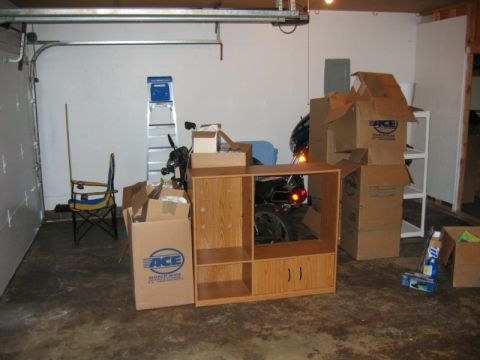 1985 Ford LTD Crown Victoria - A motorcycle is visible in a cluttered garage, partially hidden behind furniture and boxes.