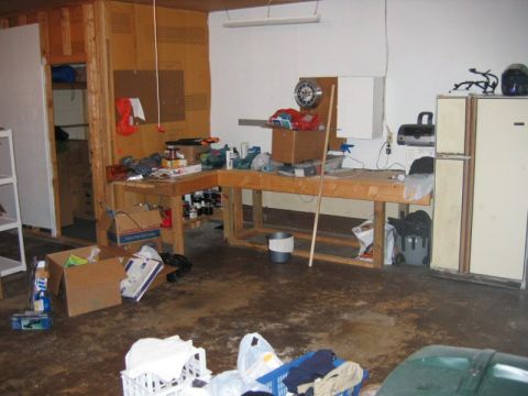 1985 Ford LTD Crown Victoria - A messy garage scene a workbench laden with tools and supplies, alongside various storage items and appliances.