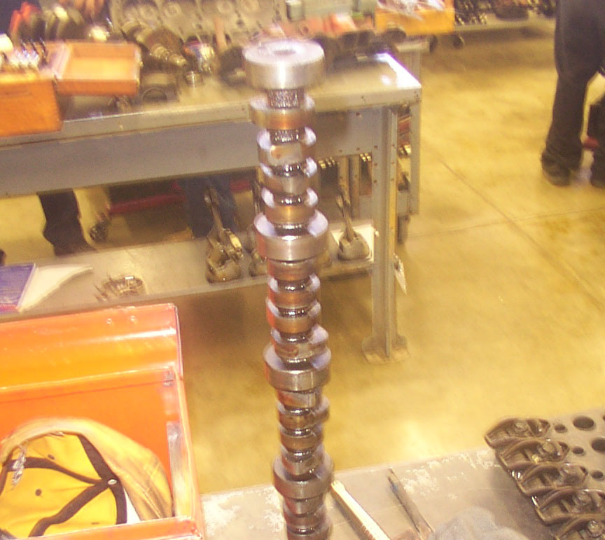 Camshaft standing upright on a workbench, with other engine parts and tools in the background