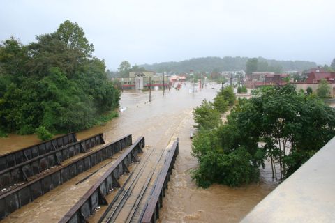 1985 Ford LTD Crown Victoria - A town street is submerged in floodwaters, with railway tracks visible in the foreground.
