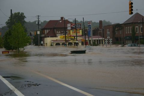 1985 Ford LTD Crown Victoria - A street is flooded, submerging cars and parts of buildings, with a Bay Shop sign visible.