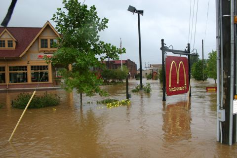 1985 Ford LTD Crown Victoria - A McDonald's restaurant is partially submerged in floodwaters, with the iconic golden arches sign visible.