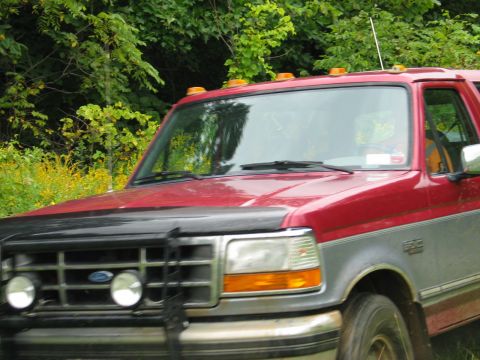 1995 Ford Bronco - Front view of a red and grey 1995 Ford Bronco parked outdoors with trees in the background.
