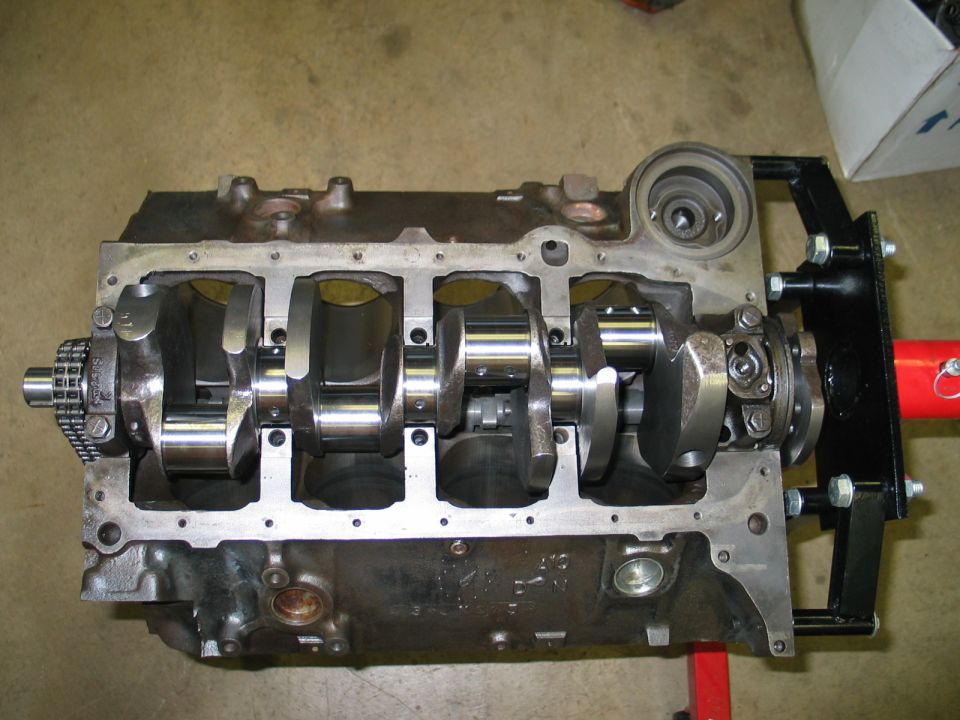 Engine block with crankshaft and timing chain visible, mounted on a stand