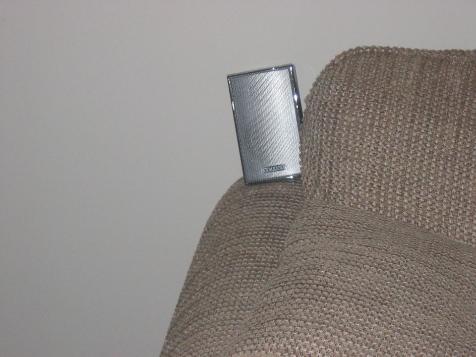 Silver rectangular speaker with textured grille attached to tan fabric
