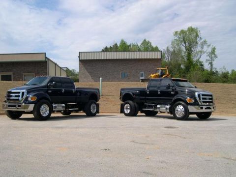 1998 Ford Taurus - Two black Ford F-650 trucks are parked in front of a building with a yellow loader in the background.