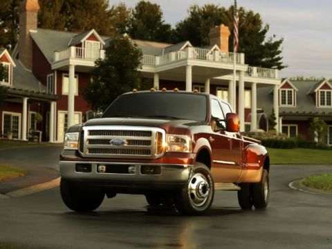 1998 Ford Taurus - A brown Ford F-350 Super Duty pickup truck is parked on a wet road in front of a large house.