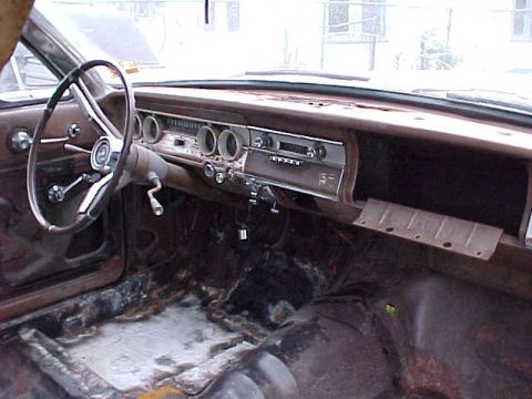 1964 Mercury Comet - The interior of a classic car shows a worn dashboard and steering wheel, with significant rust on the floor.
