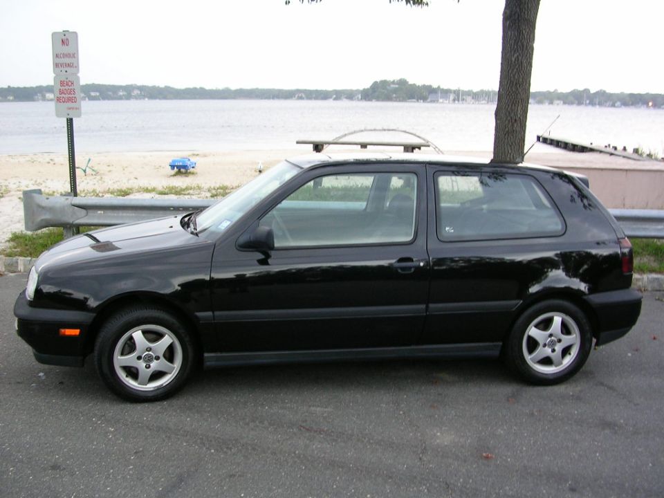 Black VW Golf Mk3 three-door hatchback in side profile parked by a bay beach