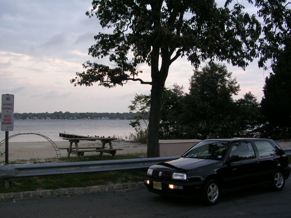 Black VW GTI hatchback parked by a guardrail at a bayside beach at dusk