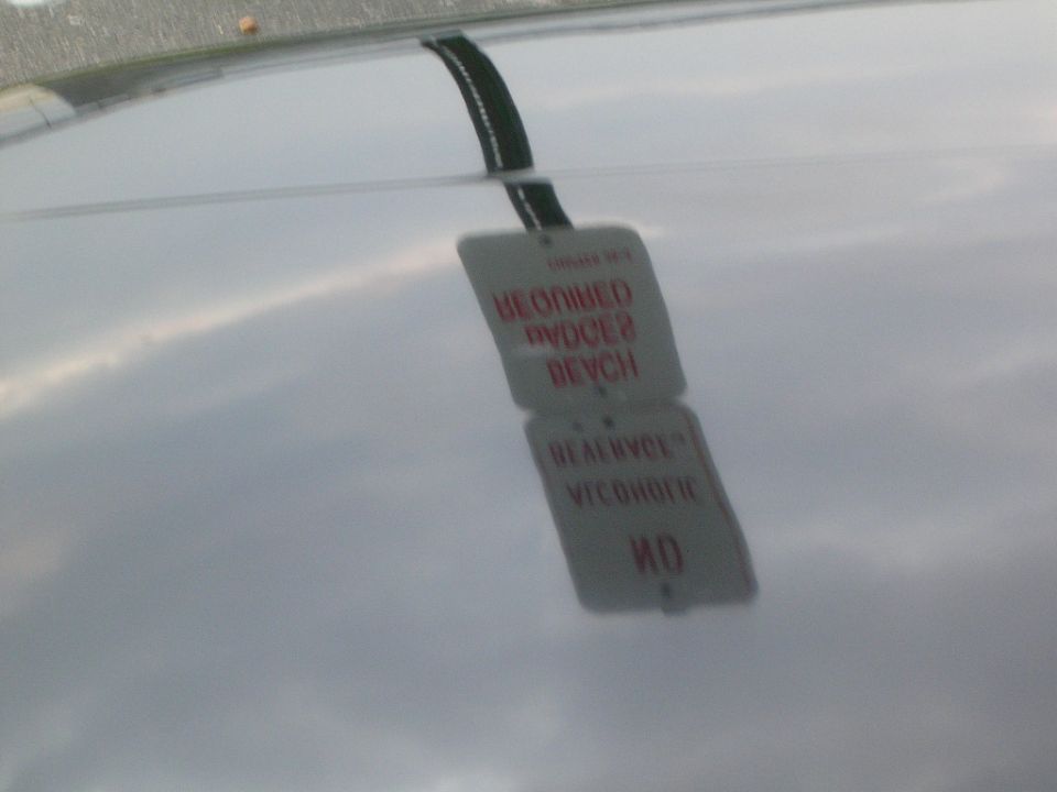 Beach parking signs reflected in the polished paint of a car's hood under a cloudy sky