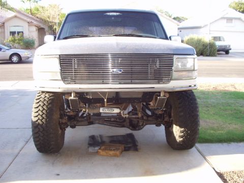 1993 Ford Bronco - This lifted Ford truck has a prominent chrome grille and visible front suspension components.