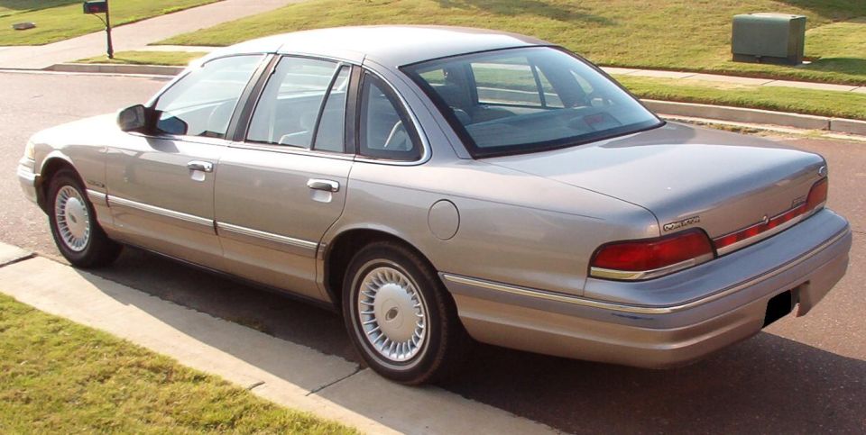 Rear-left view of a silver Ford Crown Victoria sedan parked at a curb